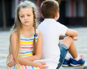 A girl and boy sat on a wall looking unhappy.